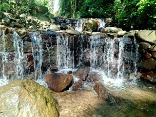 A tranquil and refreshing waterfall cascading over layered dark rocks and natural stone formations. © MohammadAshar
