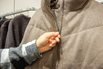 hand holding a winter coat, choosing a warm coat for winter 2027, clothes shop © Nathalie Tabak