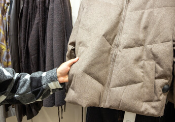 hand holding a winter coat, choosing a warm coat for winter 2027, clothes shop © Nathalie Tabak