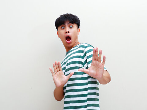 A shocked young Asian man making funny face with raised palms stop gesture against studio background for funny reaction and rejection campaign advertisement banner.