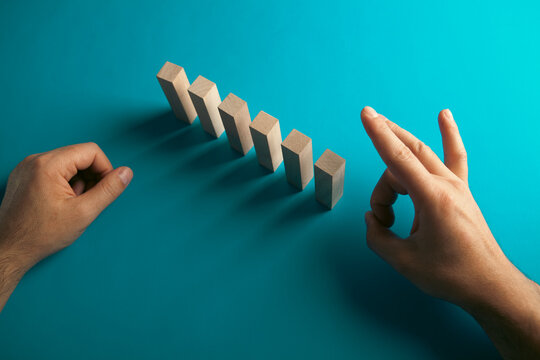 Conceptual image of domino effect. Businessman hand placing wooden block on top of dominoes.