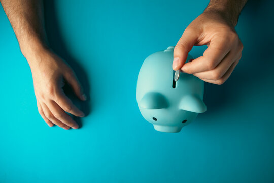 Man hand holding blue piggy bank on blue table background, saving money concept