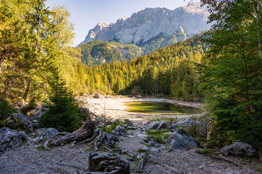 Scenic autumn view of small alpine Lake Frillensee next to Eibsee with a colorful forest at the foot of the rocky Zugspitze mountain.