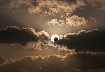 Fototapeta premium Solar eclipse and astronomy event, partial sun obscuration by moon with dramatic clouds and light rays in the sky during a rare celestial phenomenon