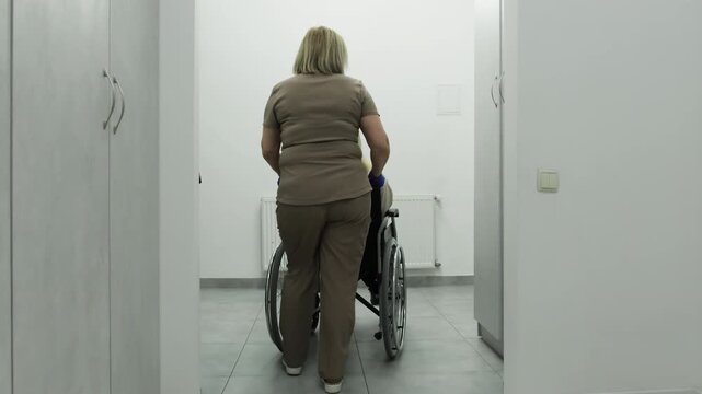 Calm nurse transports female patient past modern medical offices. Doctor and woman move toward ultrasound procedure room. Slow motion