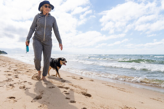 Active senior walking dog barefoot on Lake Michigan beach