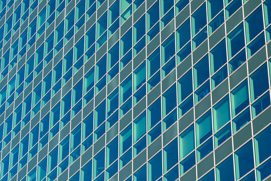 Blue glass facade with a geometric grid creating diagonal architecture across a building exterior in daylight from a close perspective