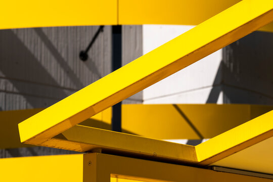 Modern architecture with yellow beams crossing a geometric facade and showing building structure from a close perspective in direct sunlight