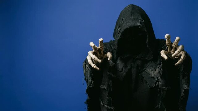Grim reaper in black hooded cloak reaching with skeleton hands on blue background. Spooky Halloween horror character. Death and fear concept. Costume, scare.