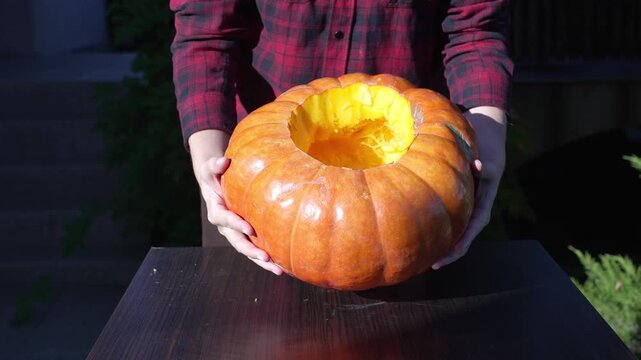 Woman holding and rotating hollow carved pumpkin showing empty interior at sunset, 4k 60fps slow motion static footage for halloween preparation