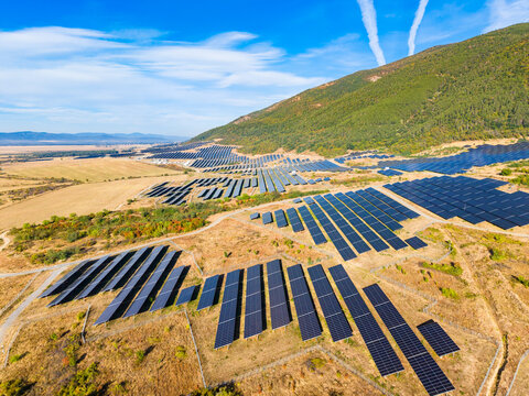 Solar panel farm located on a hillside in a rural area under a clear blue sky with some clouds observed during daylight