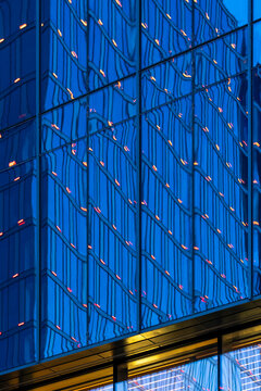 Blue tower facade with lit windows and a geometric grid creating abstract modern architecture in a vertical exterior building detail