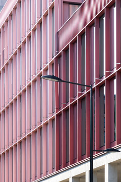 Red facade with vertical fins and linear rhythm creating abstract modern architecture around a streetlight in a geometric exterior building detail