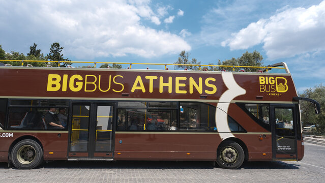 Brown double-decker sightseeing bus with passengers on open upper deck driving through Athens, Greece.