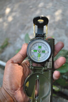 shot of a person holding a tactical military-style lensatic compass outdoors, ready for navigation. Featuring a detailed dial, sighting wire, and folding lid, this image is perfect for concepts relate