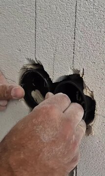 Vertical 9:16 aspect ratio shot of the installation process of a double gang electrical box into an aerated concrete wall.