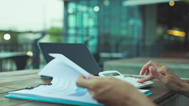 Business woman analyzes document data outdoor, reviewing financial document sheets beside tablet device where another document report rests.