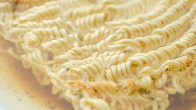 Instant ramen noodles soaking in hot boiling water with spices close up.