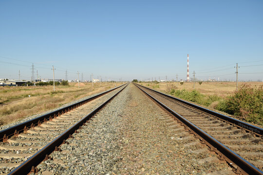 Railway line extending forward through a grassy landscape under a bright sky