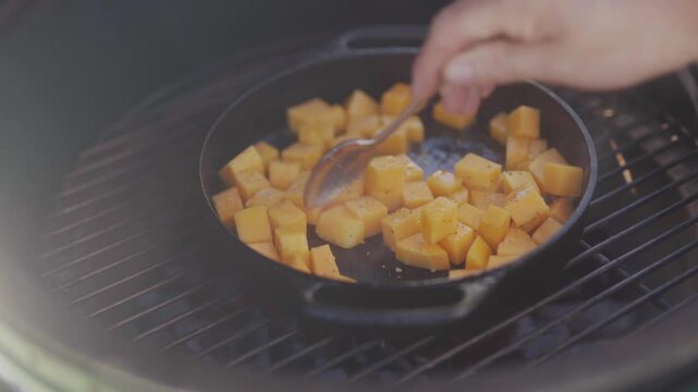 Butternut squash cubes grill over cast iron pan on outdoor kitchen