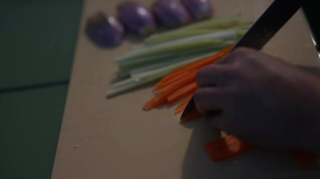 Hand slices carrots and celery on a wooden cutting board