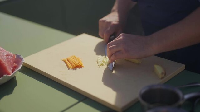 Chef prepares ginger slices on a wooden cutting board in an outdoor kitchen