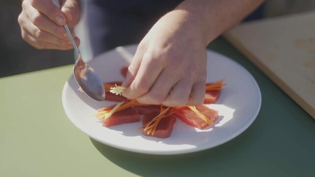 Hands plating a vibrant dish with a spoon on a white plate