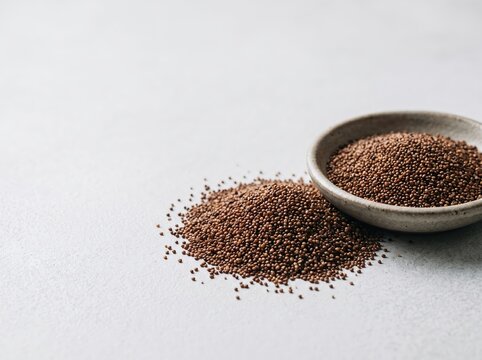 Bowl of brown seeds spilled on light textured surface