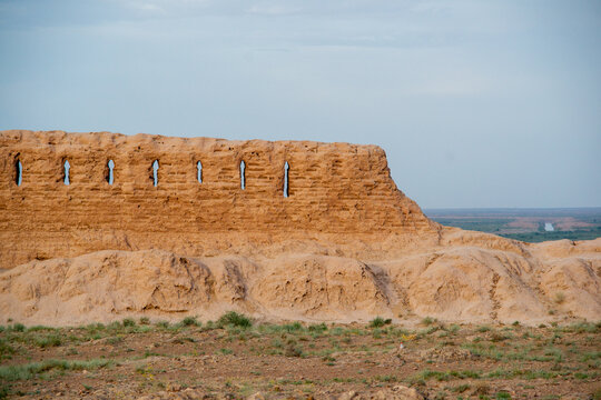 Ancient ruins of the mud-brick walls of the Ayaz-Kala fortress set in a desert landscape, featuring narrow lancet windows and a distant horizon. Uzbekistan.