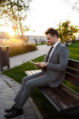 Businessman sits on bench using tablet in park during sunset © Marko