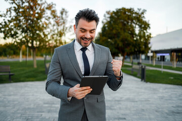 Man in suit smiles while using tablet in outdoor park area during day © Marko
