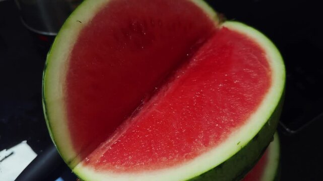 Cut watermelon rests open on dark kitchen surface, its juicy red flesh and pale rind suggesting summer refreshment. Fresh melon offers cooling, hydrating choice for warm weather, with cut flesh