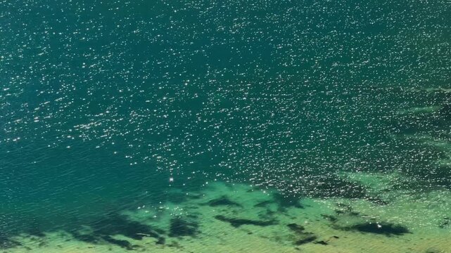 Direct overhead shot captures bright sunlight glistening on gentle ripples of turquoise alpine lake water in cordillera huayhuash region during peruvian andes mountain adventure trekking
