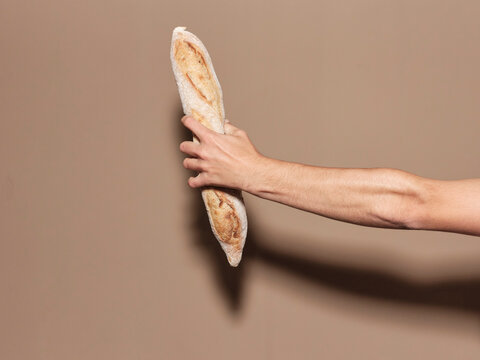 A hand holding a baguette against brown background