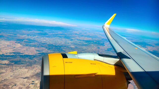 View from airplane window of Ryanair aircraft wing and engine flying over countryside during flight.