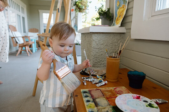 Candid baby painting with large brush on porch