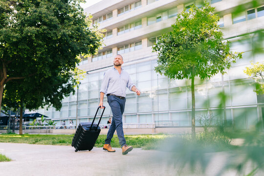 Businessman pulling luggage walking along modern city building