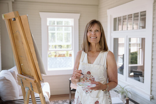 Smiling mature woman painting at an easel in a bright studio