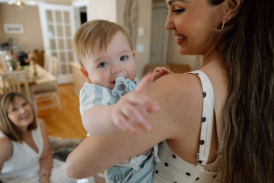Candid mother holding baby with grandmother smiling nearby