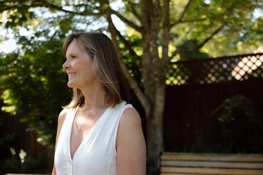 Candid outdoor portrait of a smiling mature woman in sunlit gard