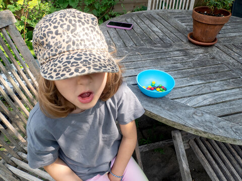 Young girl in a leopard print hat sitting at a backyard table