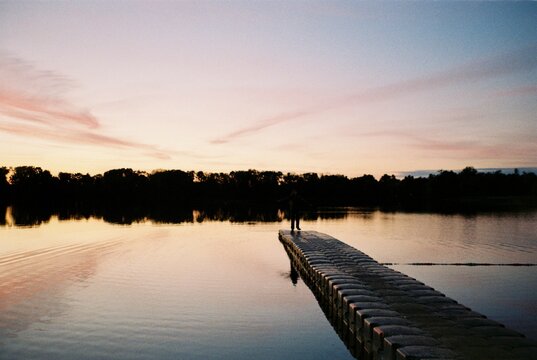 Lone Figure on a Jetty at Sunset over a Still Lake