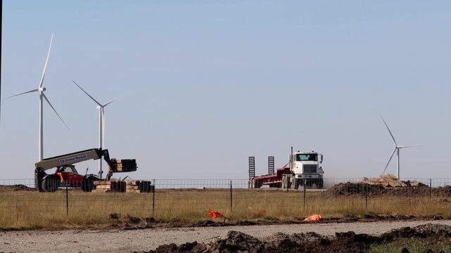 Loader loading a flatbed trailer near Kansas wind turbines