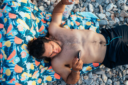 man relaxing on a colorful towel on a rocky beach