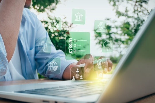 Businessman typing on laptop with digital ESG environmental, social, and governance icons and sustainability interface in outdoor nature setting, concept of corporate responsibility and green business