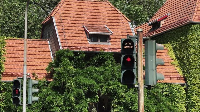Car passing on street with visible pedestrian red light lit up on a street corner in Germany. The street is lined with trees and houses