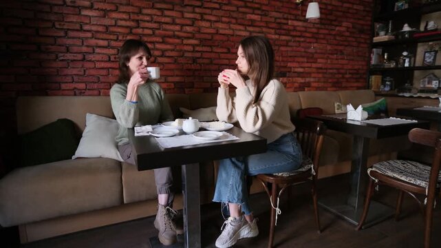 Adult daughter and her senior mother spending time together, sitting at a table in a cozy cafe, drinking coffee and talking, enjoying pleasant conversation and family bonding moments