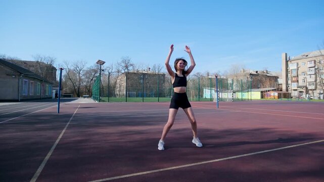 Athletic young student doing jumping jacks on an outdoor basketball court. Sporty female teenager in activewear performing cardio exercises for a healthy lifestyle on a sunny day