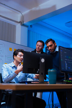 IT professional team reviewing program source code and discussing workflow on computer screen in modern high tech workspace with blue lighting