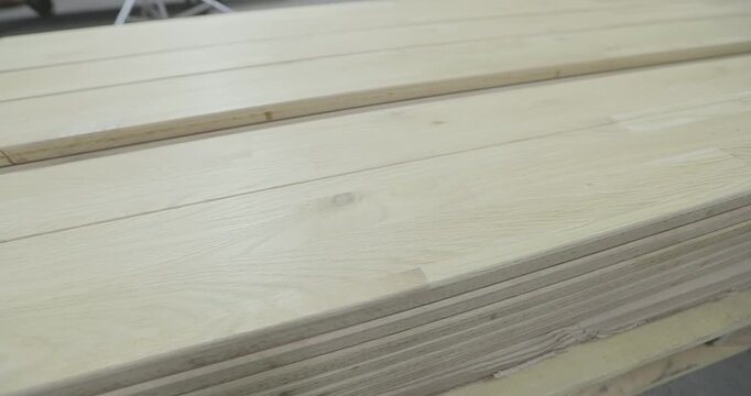 Light-colored long lumber with a natural wood texture is prepared for further processing, furniture making. A stack of wooden boards or a furniture panel for woodworking on the floor. Indoors